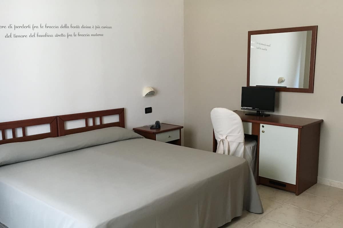 Une chambre d’hôtel comprenant un lit, un bureau avec un ordinateur, une chaise et un petit placard.
