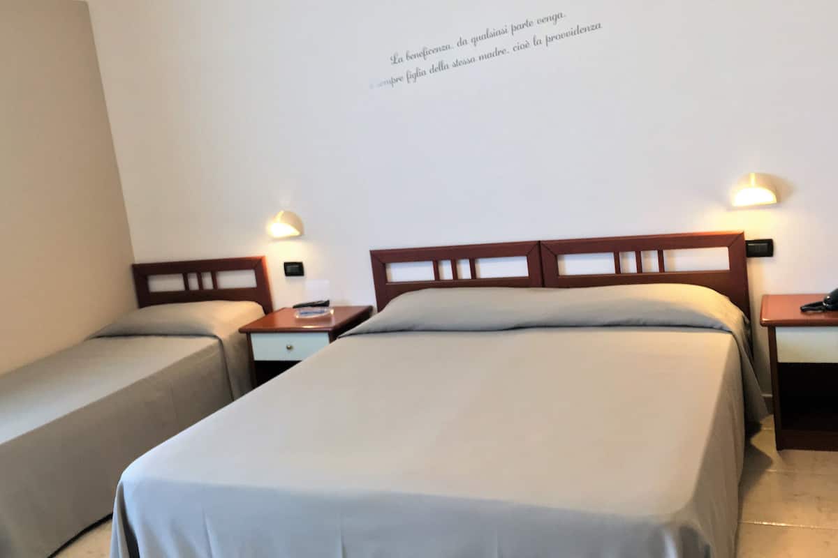 Une chambre d’hôtel avec deux lits simples, une table de chevet avec une lampe et un mur orné d’une citation.