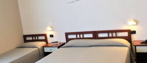 A hotel room with two single beds, a nightstand with a lamp, and a wall with a quote.