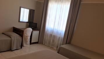A hotel room with two beds, a desk, a chair, a television, and a window with curtains.