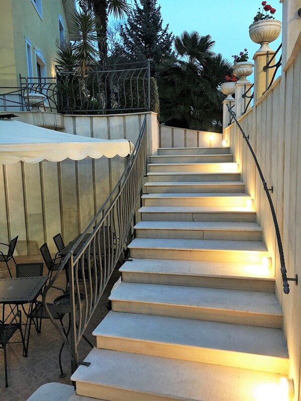 Una escalera con barandilla que conduce a un espacio exterior cubierto con sillas y mesas.