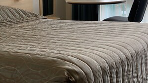 A hotel room with a large bed, a small table, a chair, a nightstand, and a window with curtains. - Shellharbour Resort (Shellharbour)