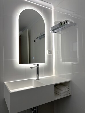 A modern bathroom with a white vanity, a large mirror with integrated lighting, and a towel rack.