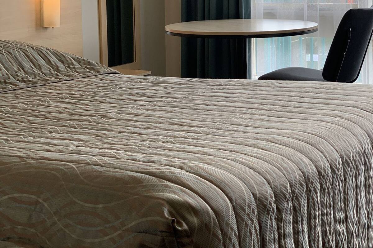 Ein Hotelzimmer mit einem Bett, einem kleinen Tisch, einem Stuhl, einer Wandlampe und einem Fenster mit Vorhängen.