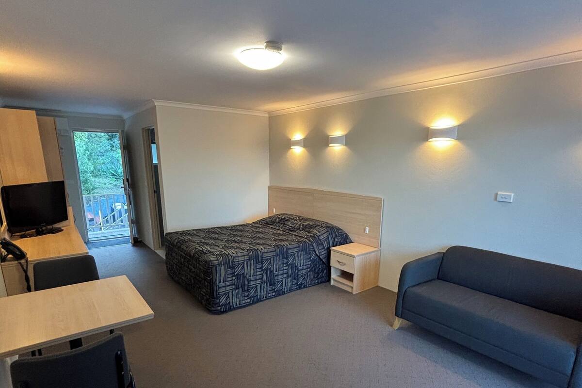 Ein gemütlicher Raum mit einem Bett, einer Schlafcouch, einem Schreibtisch mit Stuhl und einem Fernseher.