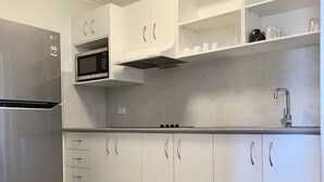 A modern kitchen with white cabinets, a stainless steel refrigerator, a microwave, and a gas stove. - Shellharbour Resort (Shellharbour)