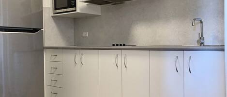 A modern kitchen with white cabinets, a stainless steel refrigerator, a microwave, and a gas stove.