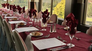 A long dining table set with red napkins, wine glasses, and plates, overlooking a scenic view. - Shellharbour Resort (Shellharbour)