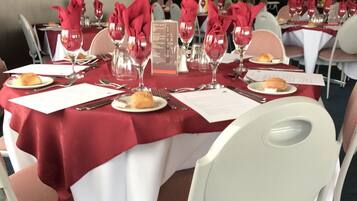 A dining area with round tables covered in white tablecloths and red napkins, set with wine glasses, plates, and cutlery.