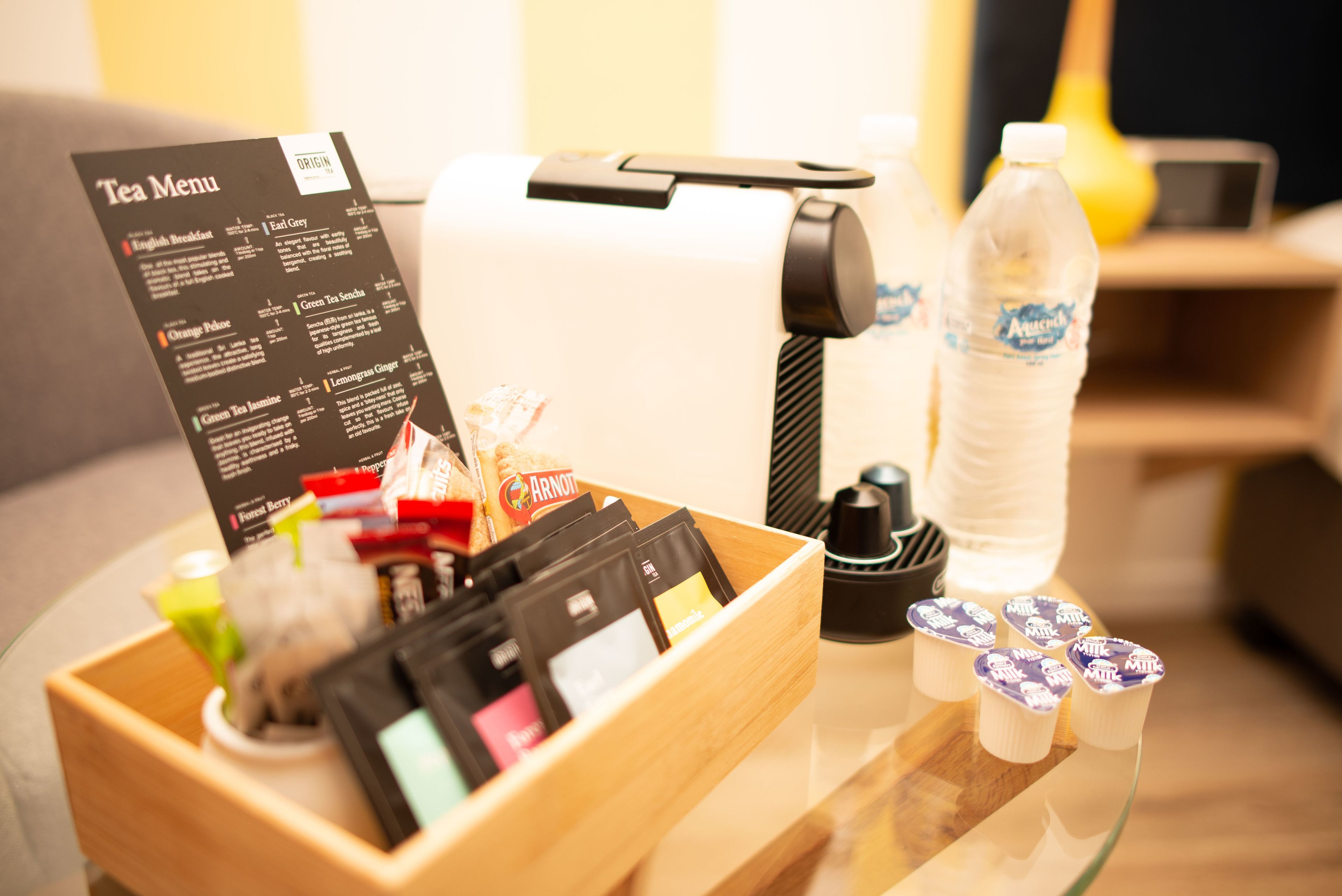 A tea menu, a coffee machine, a water bottle, and tea bags on a table.