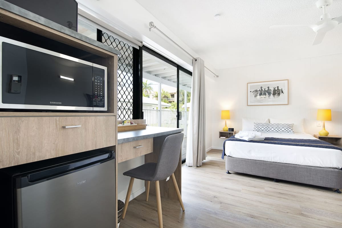 A modern hotel room with a kitchenette, a bed with a view, and a desk with a chair.