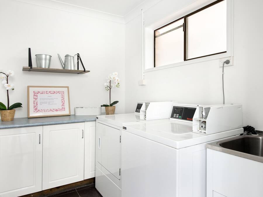 Una cocina moderna con armarios blancos, lavadora integrada, un lavabo y una ventana sobre la encimera.