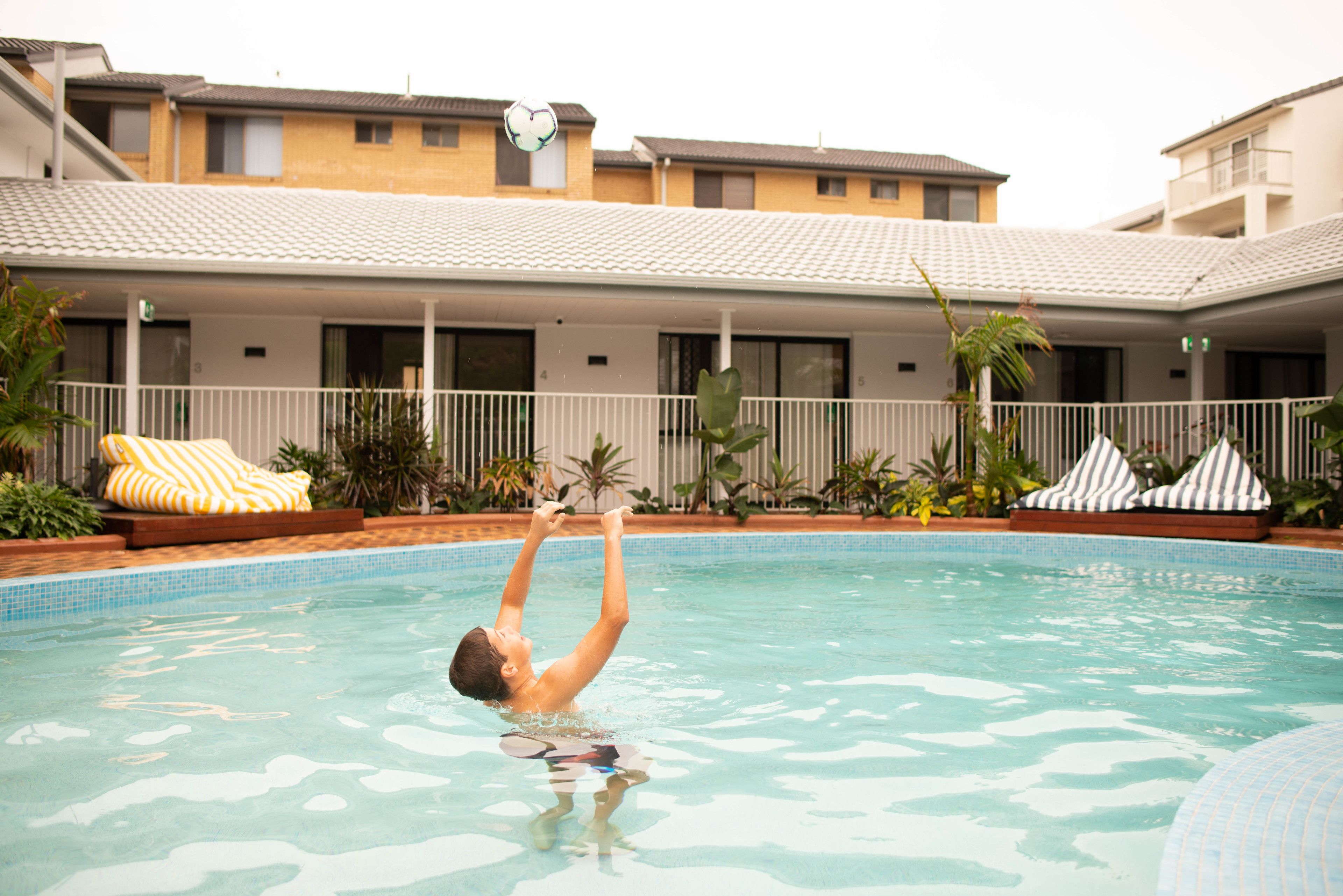 A swimming pool with a person diving. There are lounge chairs and plants around the pool.