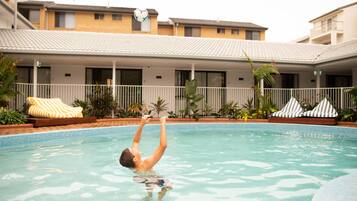 A swimming pool with a person diving. There are lounge chairs and plants around the pool.