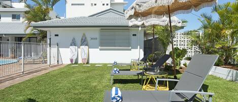 A poolside area with lounge chairs, a beach umbrella, and a sign indicating a beach.