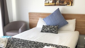 A neatly made bed with a geometric patterned bedspread, a blue pillow, and a white pillow. - Tamworth Central Motel (South Tamworth)
