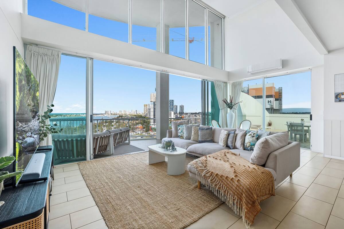 A spacious living room with a large balcony, a sofa set, a coffee table, and a view of the cityscape.