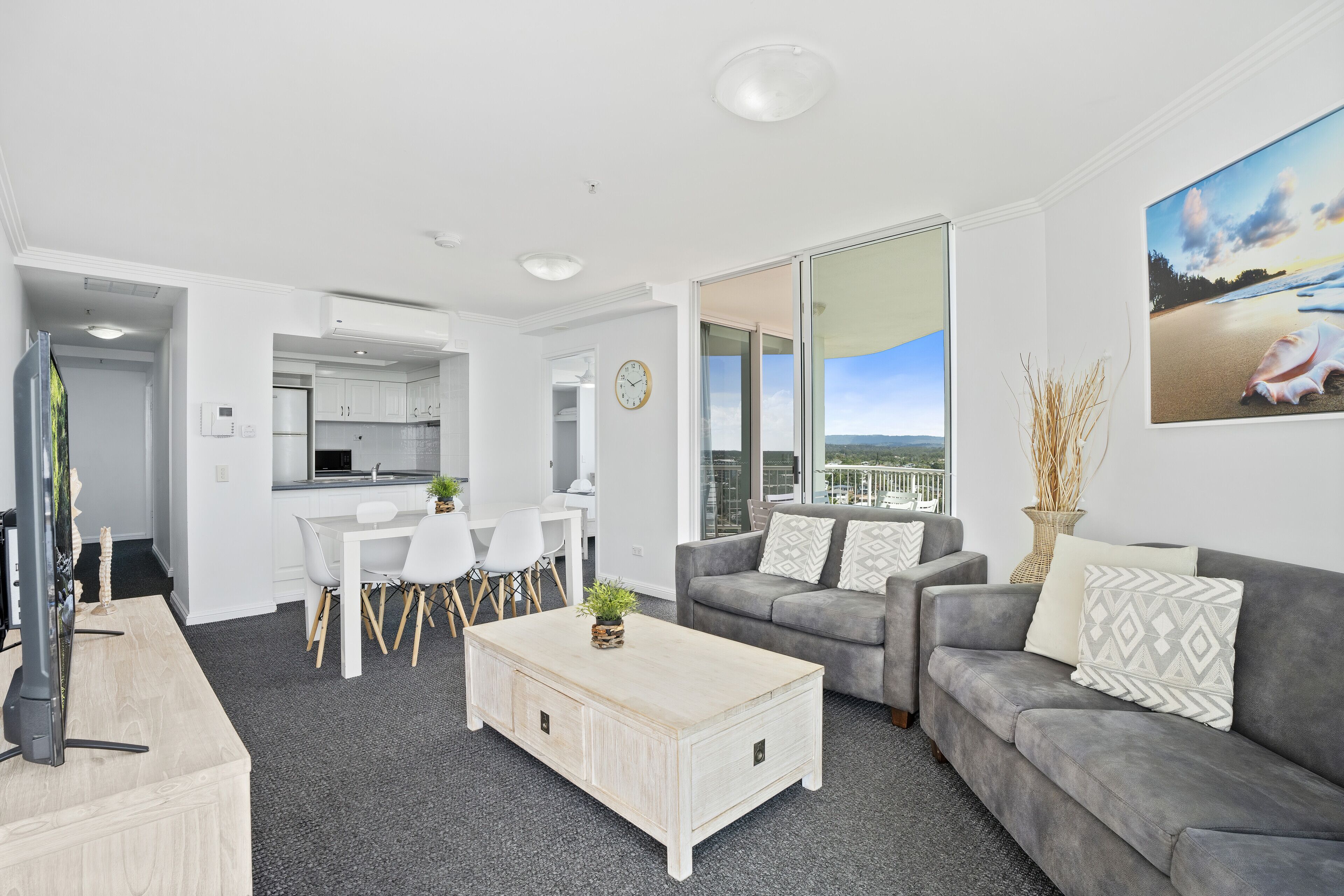 A modern living room with a grey sofa, a white coffee table, and a dining area with a white table and chairs.