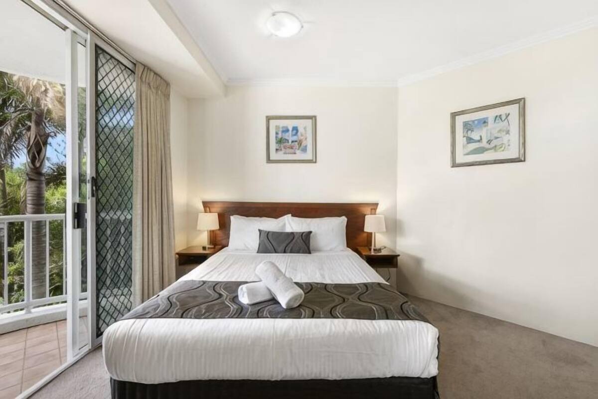 A hotel room with a large bed, two bedside tables with lamps, a sliding glass door to a balcony, and two framed pictures on the walls.