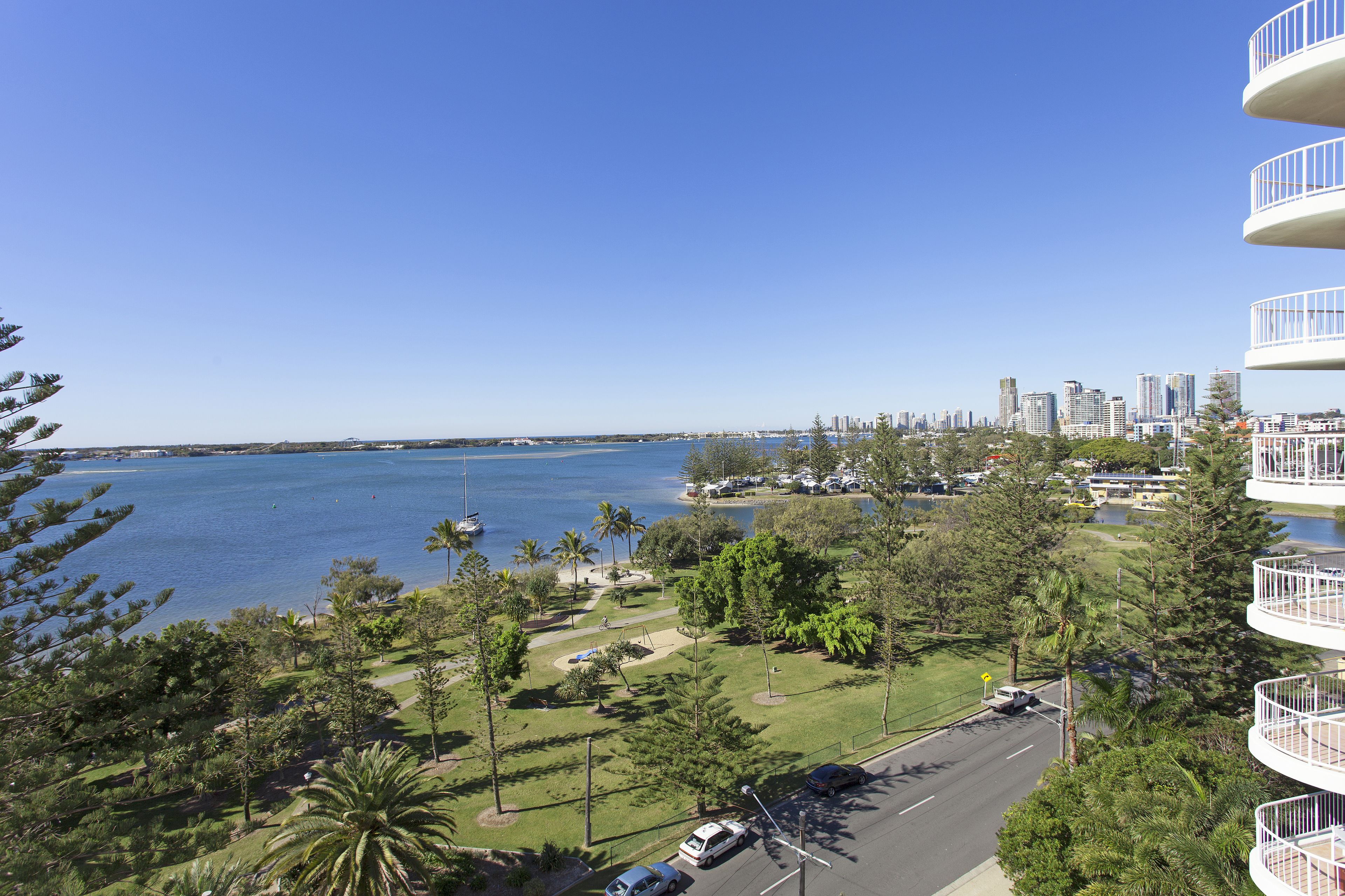 A high-rise building with balconies overlooking a coastal area with a road and greenery.