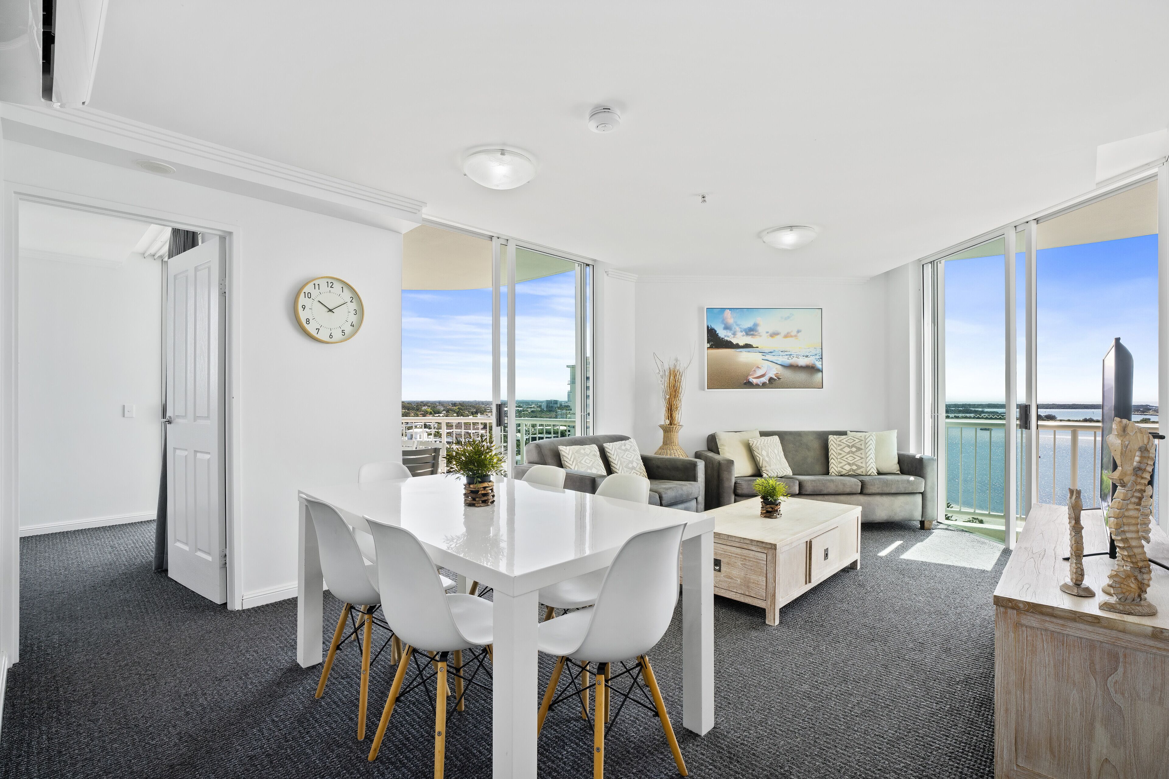 A modern living room with a dining area, large windows, and a view of the sea.