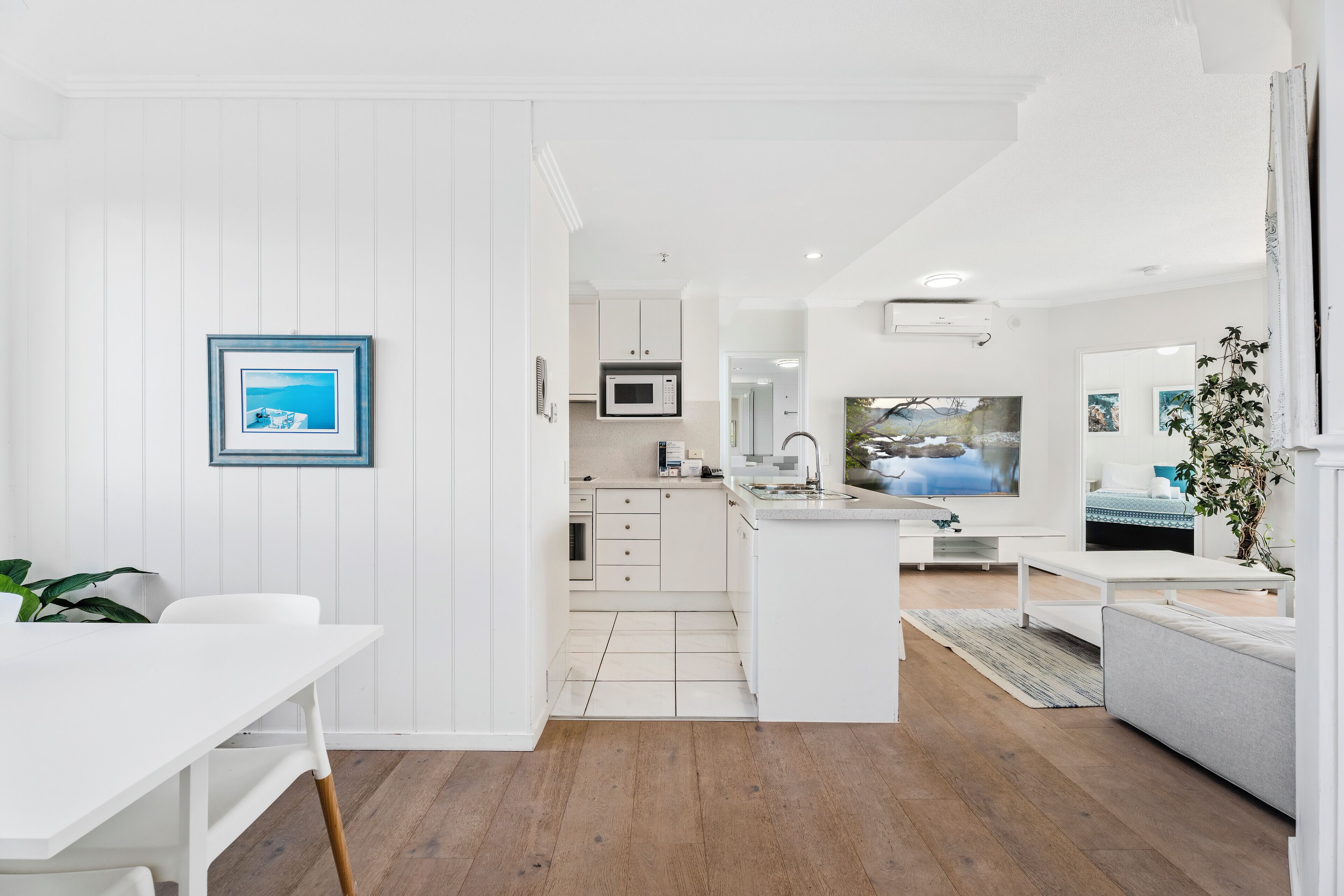 A modern kitchen with white cabinetry, a microwave, and a dining area with a white table and chairs.