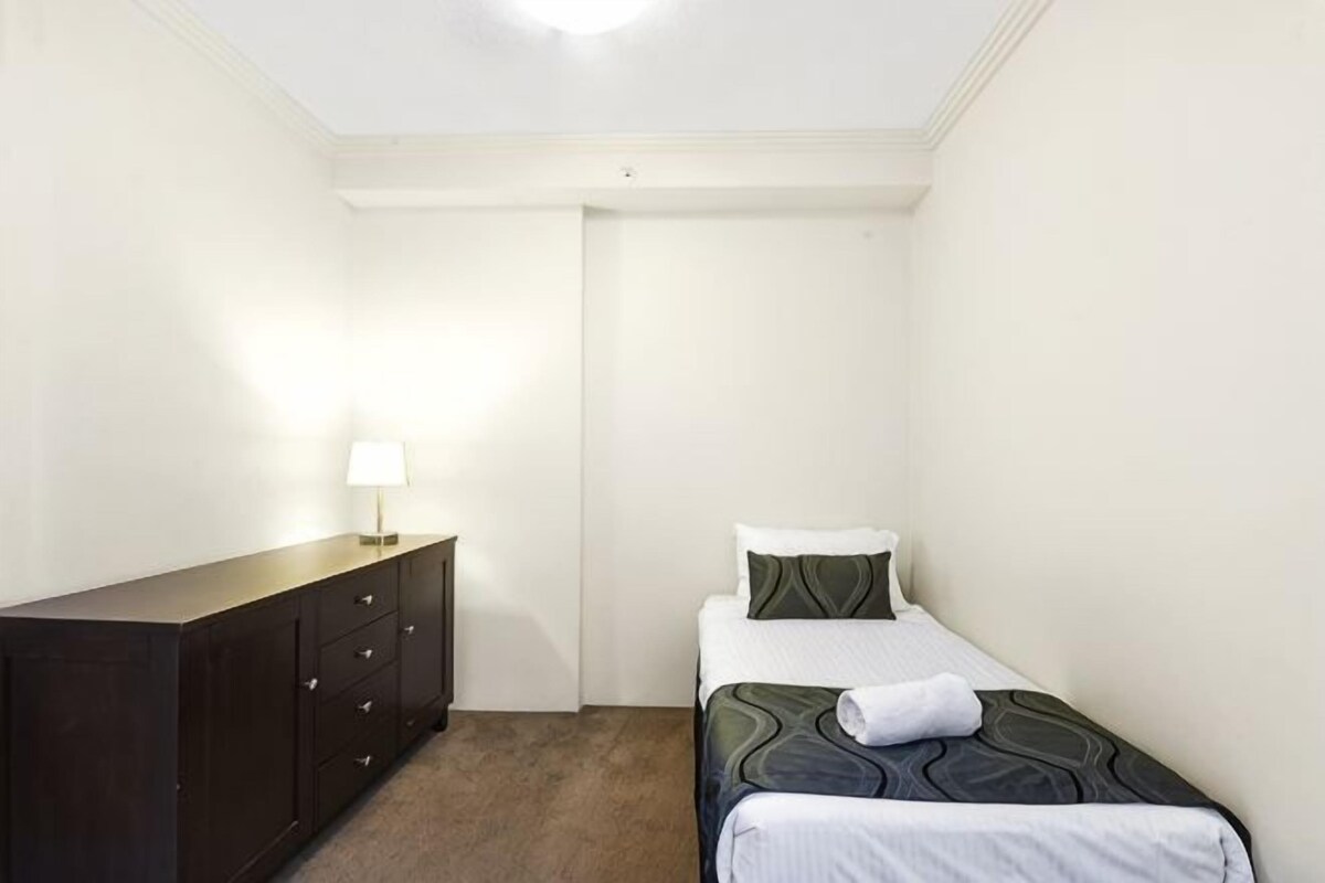A small, clean room with a bed, a dresser, and a lamp.