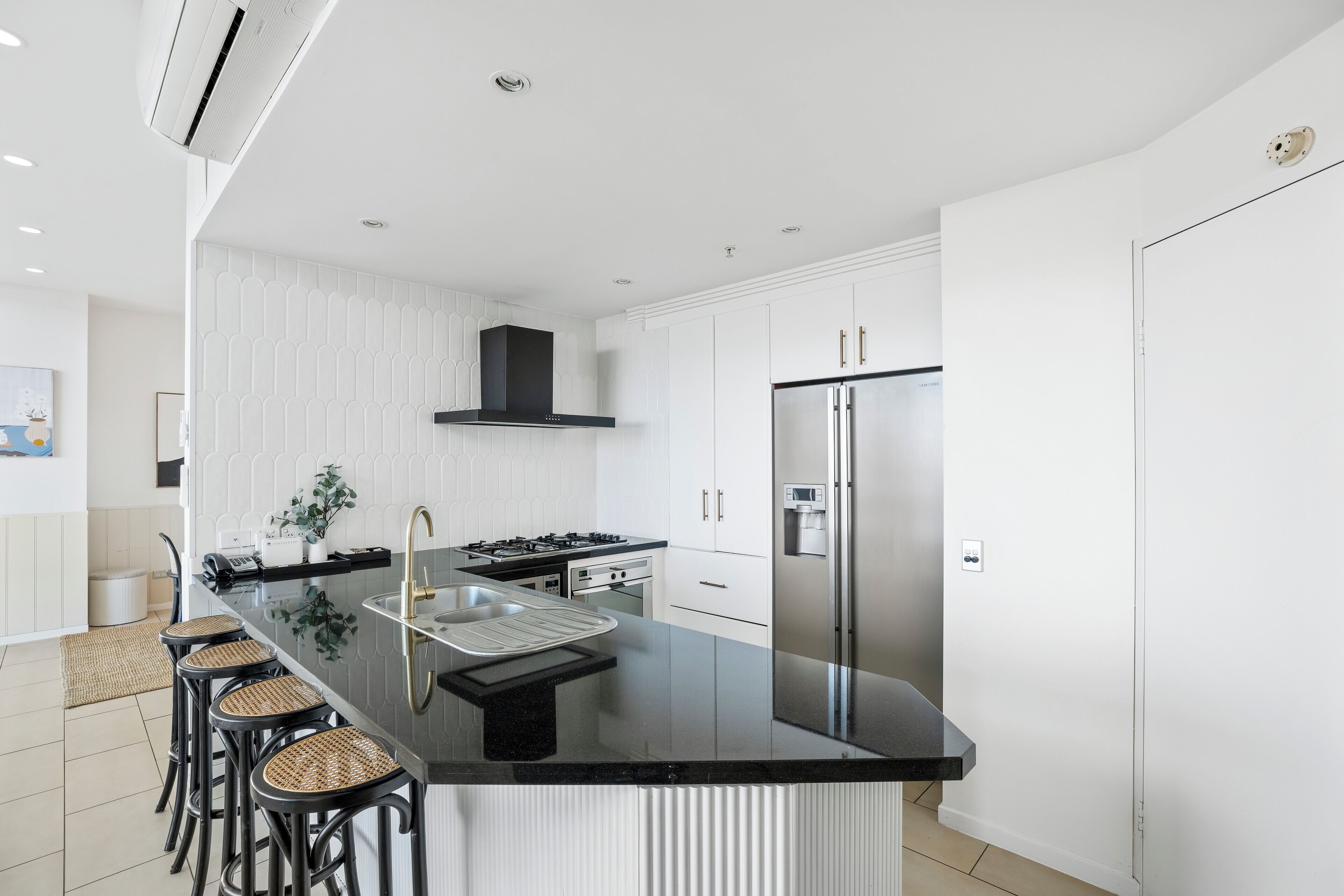 Een moderne keuken met een centraal eiland, roestvrijstalen apparatuur en een witte achterwand.