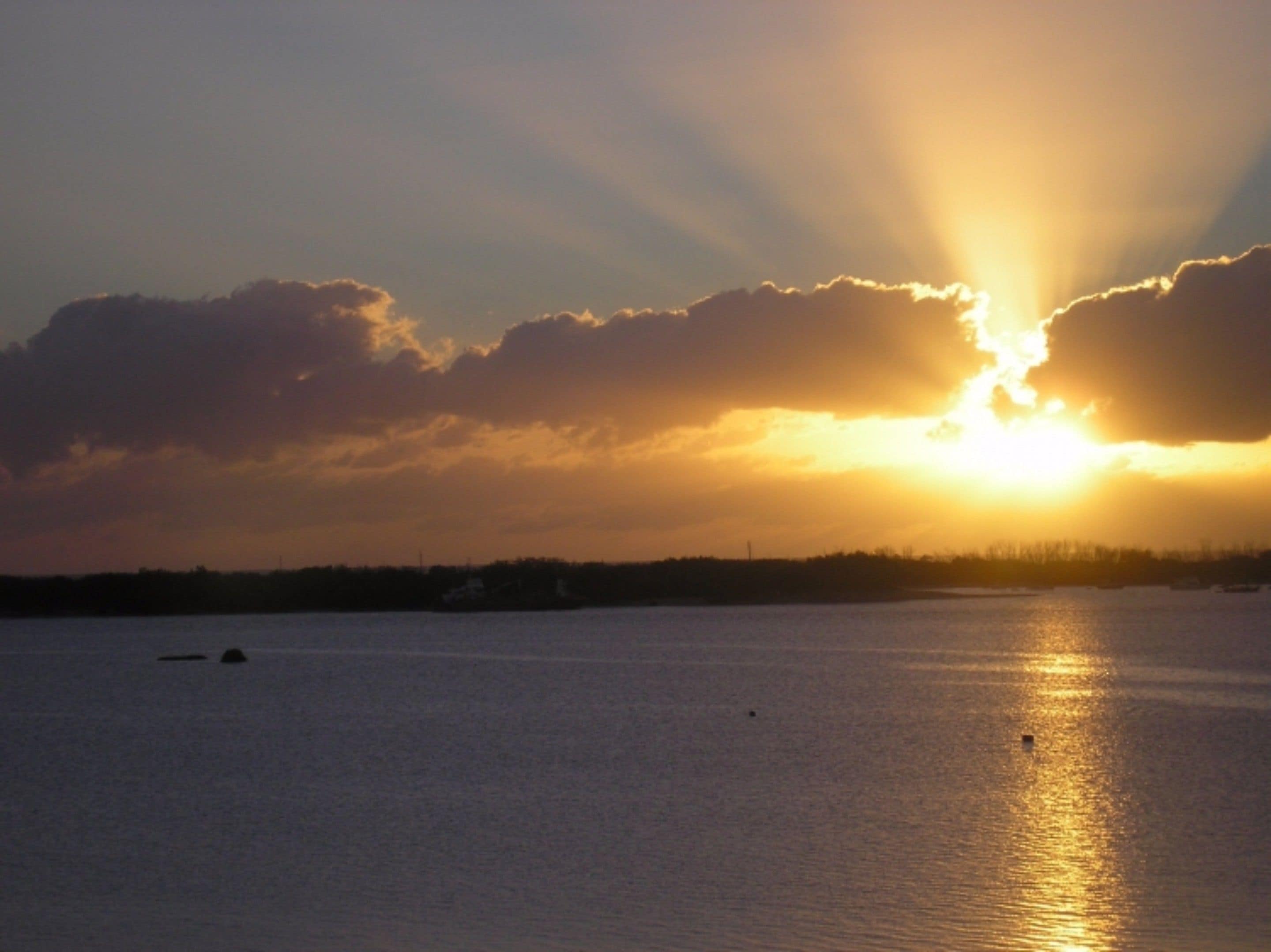 Un atardecer sobre una masa de agua con barcos y una costa lejana.