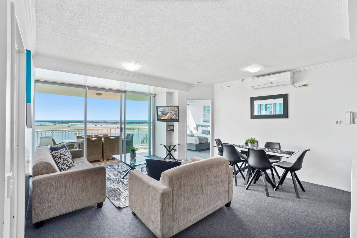 A modern living room with a balcony, a dining area, and a TV mounted on the wall.