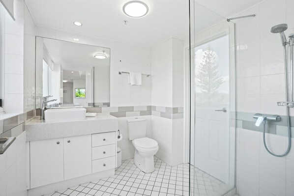A modern bathroom with a glass shower enclosure, a white toilet, and a vanity with a mirror. - Crystal Bay on the Broadwater (Labrador)