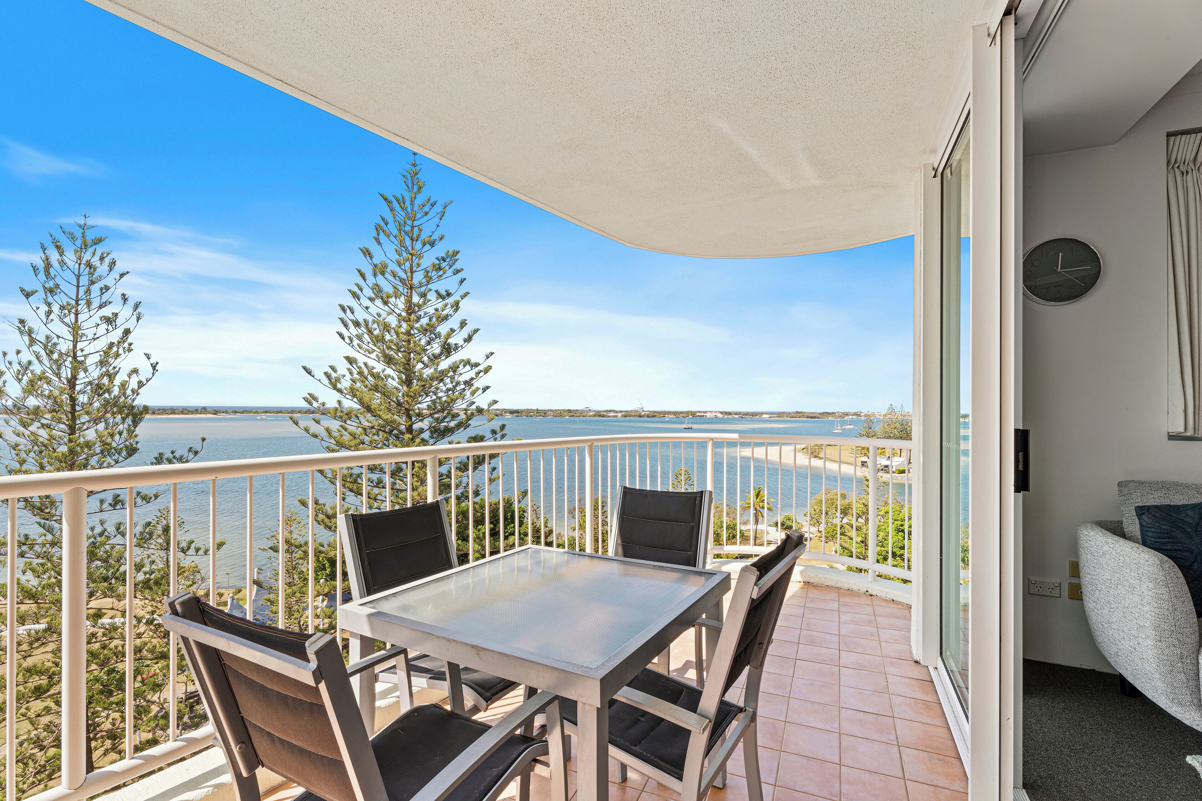A balcony with a table and chairs, overlooking a body of water and trees.