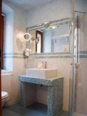 A bathroom with a white sink, a mirror with a round mirror above it, and a shower area. - Hotel Figo (Bad Kreuznach)