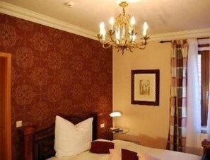 A hotel room with a bed, a chandelier, a framed picture on the wall, and a window with curtains. - Hotel Figo (Bad Kreuznach)