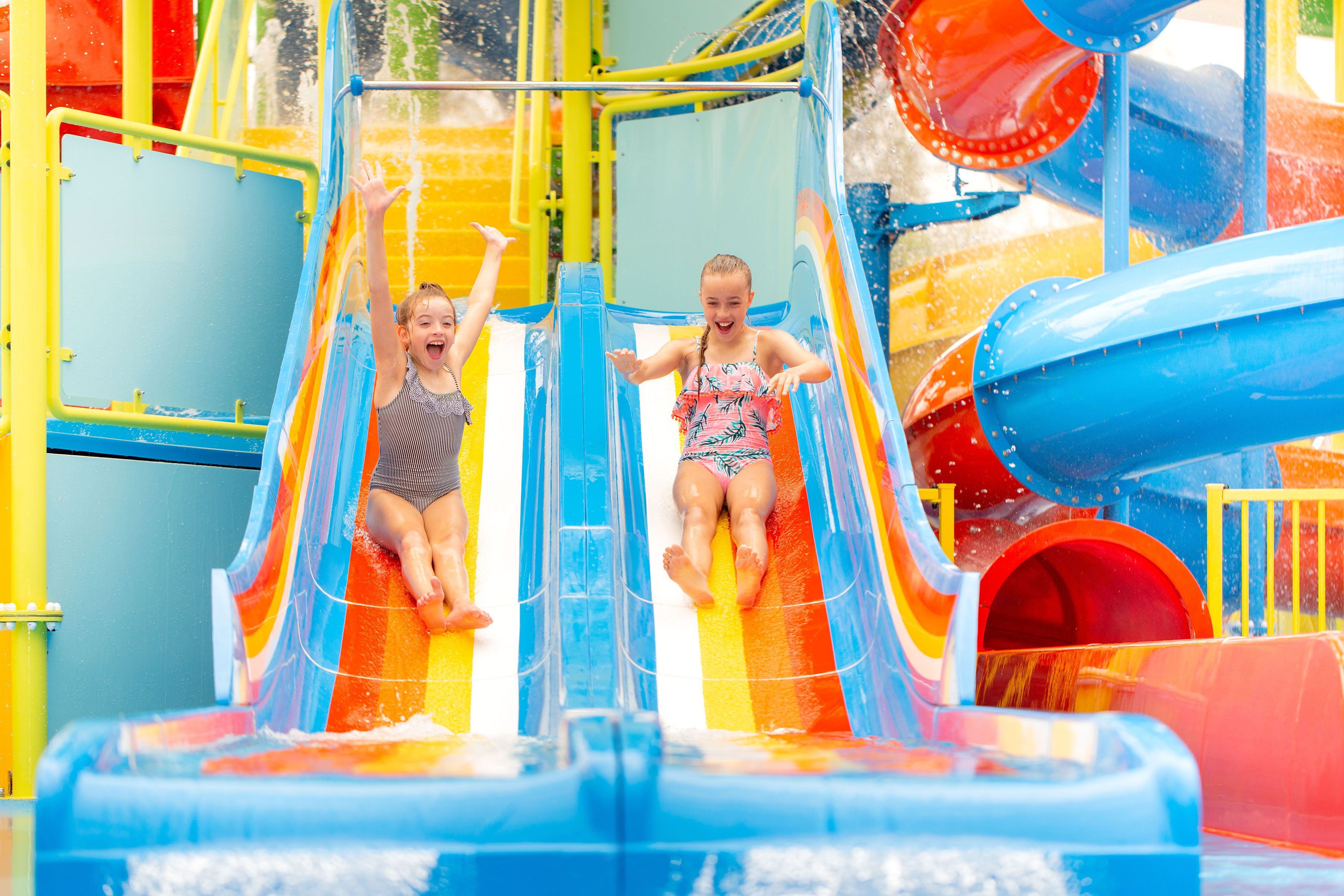 Two children sliding down a colorful water slide at a water park.