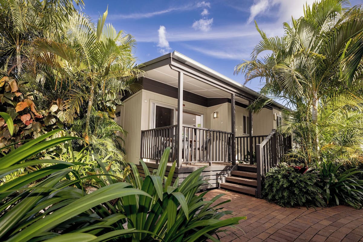 A house with a covered porch, surrounded by lush tropical vegetation.