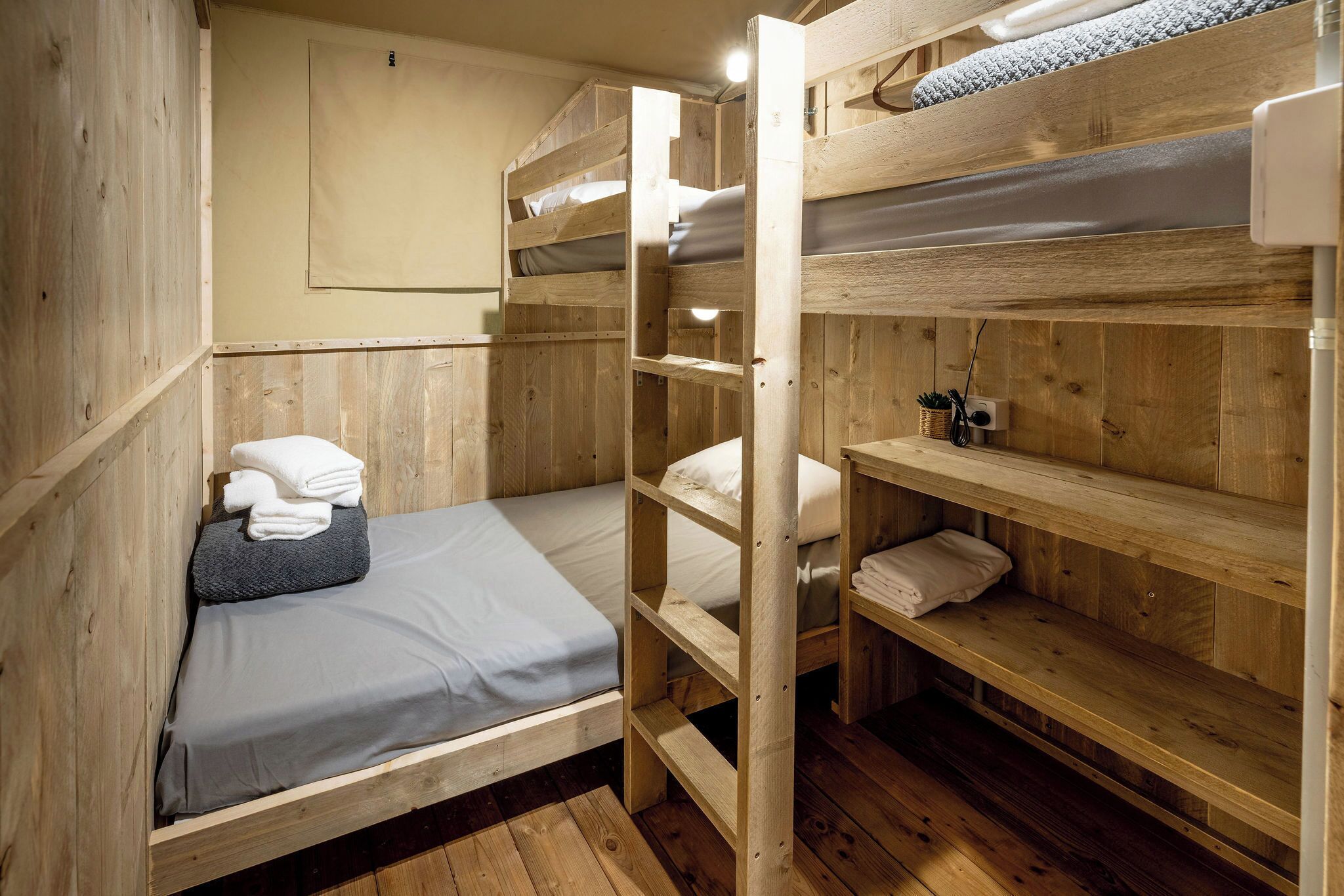 A bunk bed room with wooden walls, a single bed, and a shelf with towels.