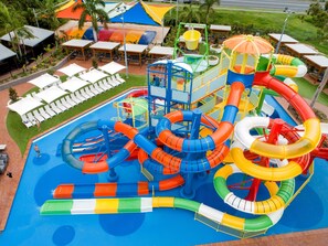 Un parque acuático con varias toboganes y piscinas, rodeado de sillas de descanso y sombrillas.