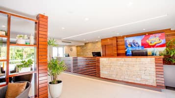 A hotel reception area with a wooden reception desk, stone wall, and potted plants.