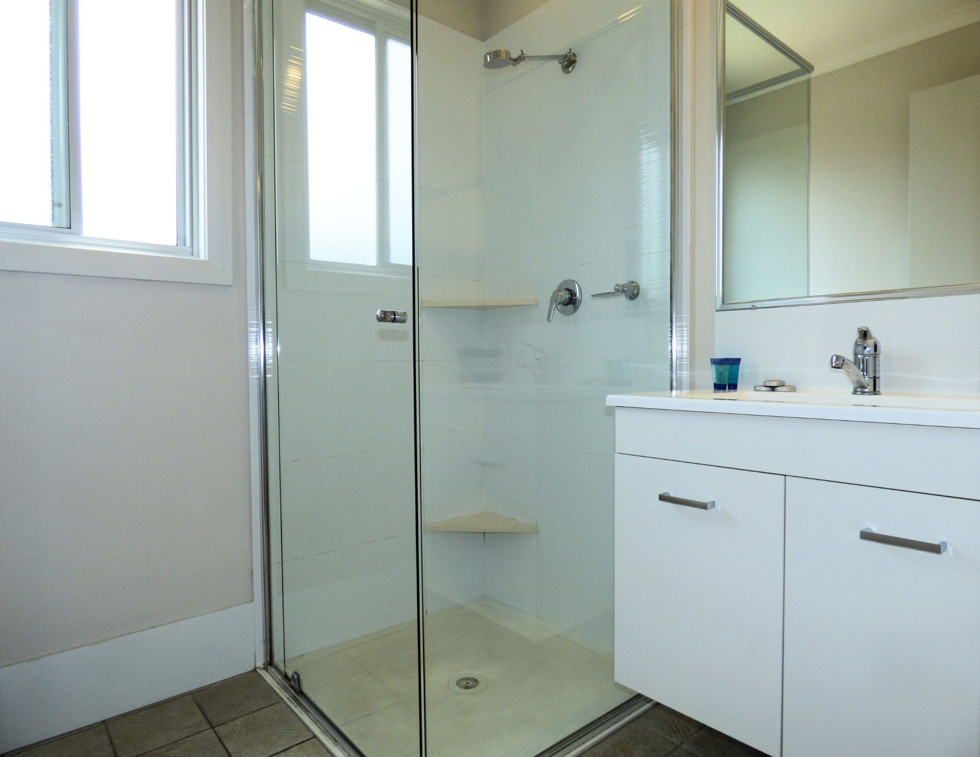A bathroom with a glass shower enclosure, a white sink, and a mirror above the sink.