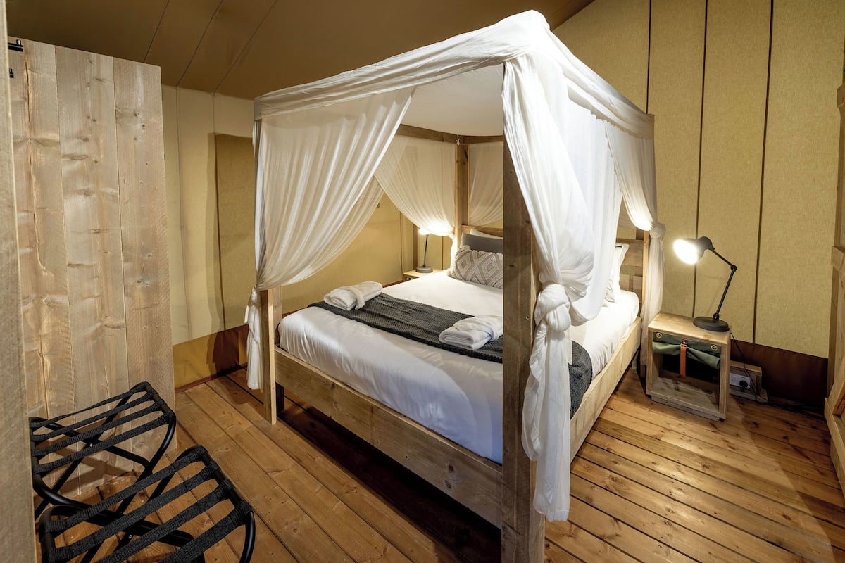 A wooden four-poster bed with white linens, a bedside lamp, and a small table with a lamp.