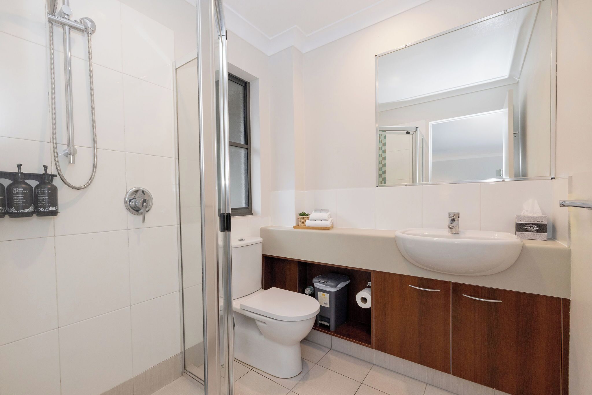 A modern bathroom with a glass-enclosed shower, a white toilet, a sink with a mirror above it, and a cabinet below.