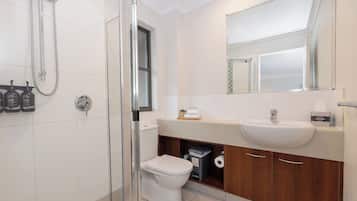 A modern bathroom with a glass-enclosed shower, a white toilet, a sink with a mirror above it, and a cabinet below.