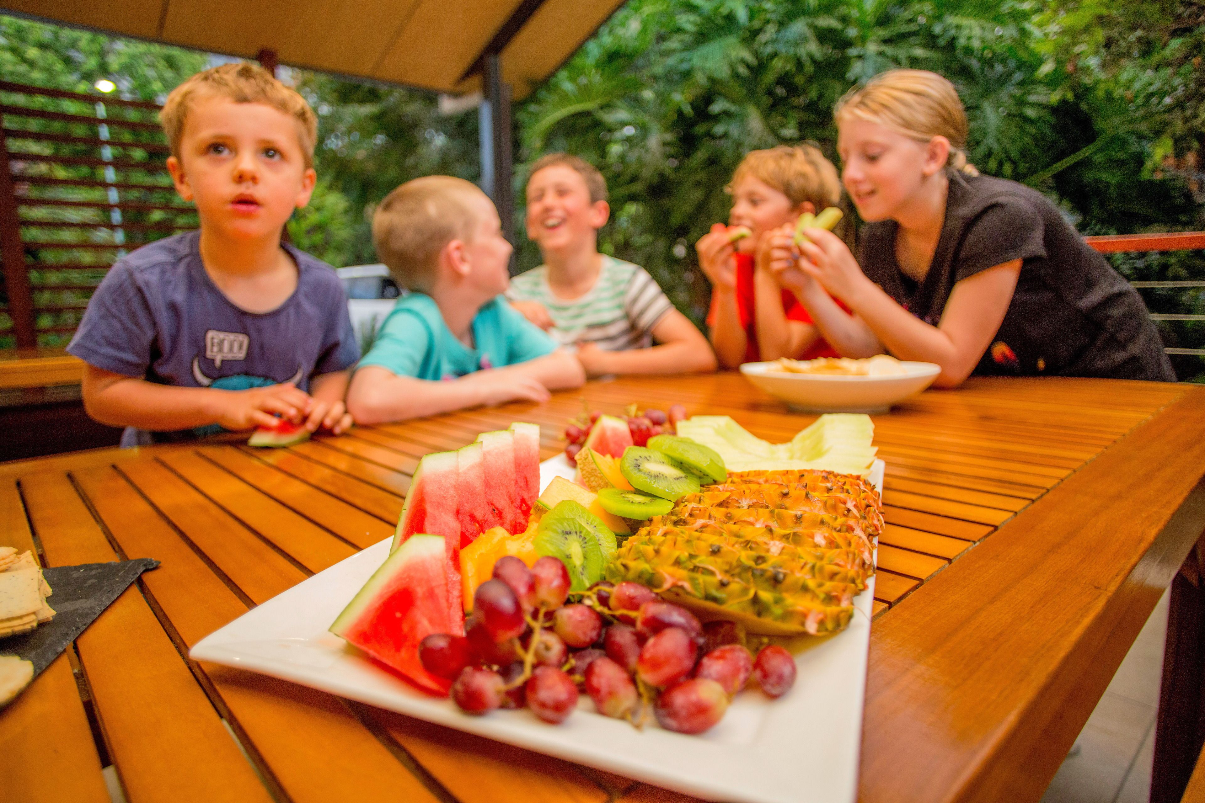 Un groupe de personnes est assis autour d’une table en bois, devant laquelle se trouve une assiette de fruits.