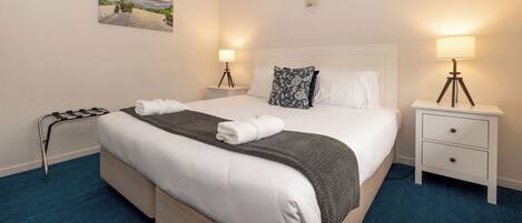 A hotel room with a large bed, two bedside tables with lamps, a painting on the wall, and a blue carpet.