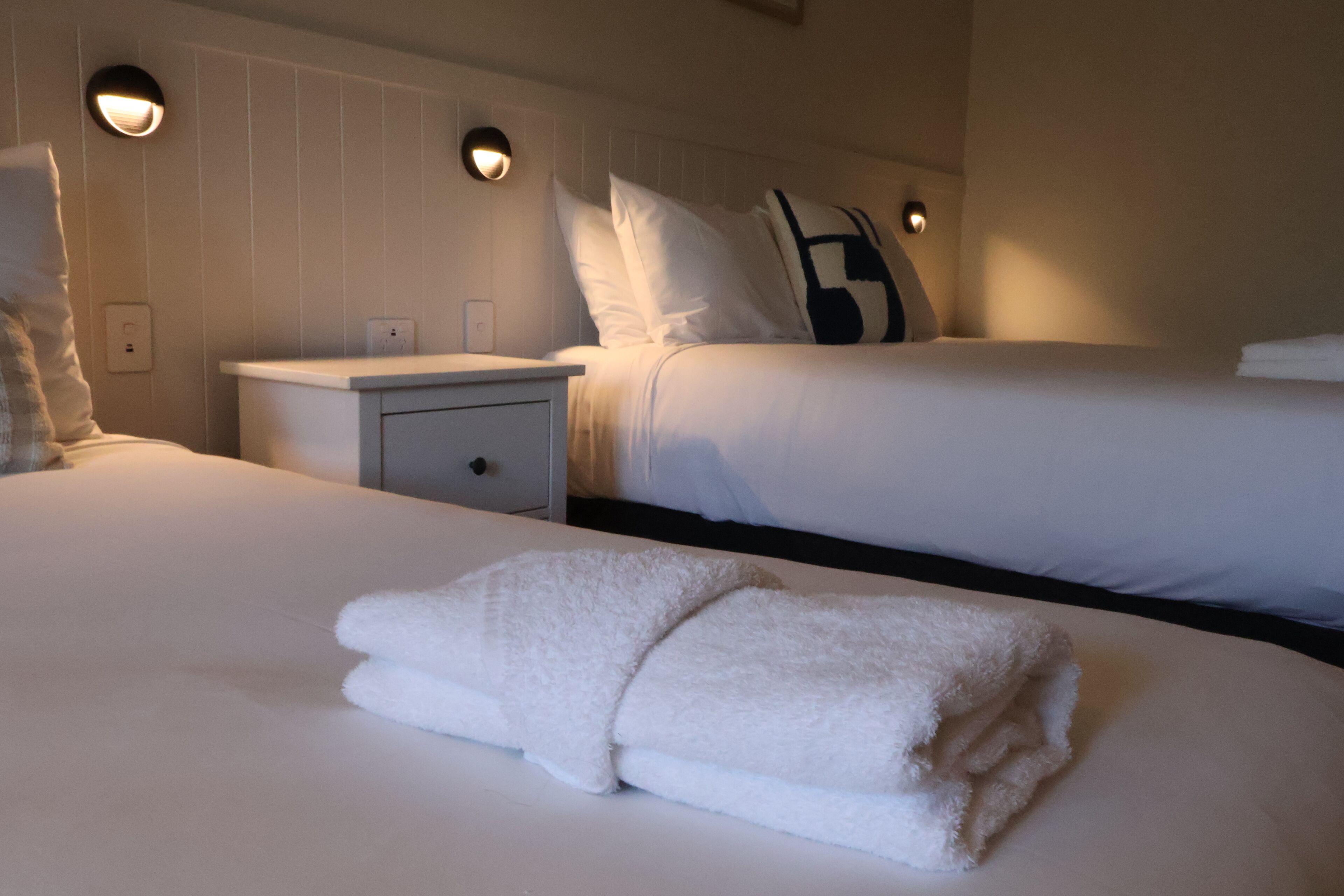 A hotel room with a large bed, a bedside table, and two wall-mounted light fixtures.