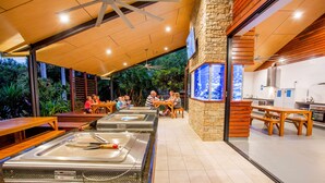 A buffet area with multiple serving stations, wooden tables, and a stone wall with a large aquarium.