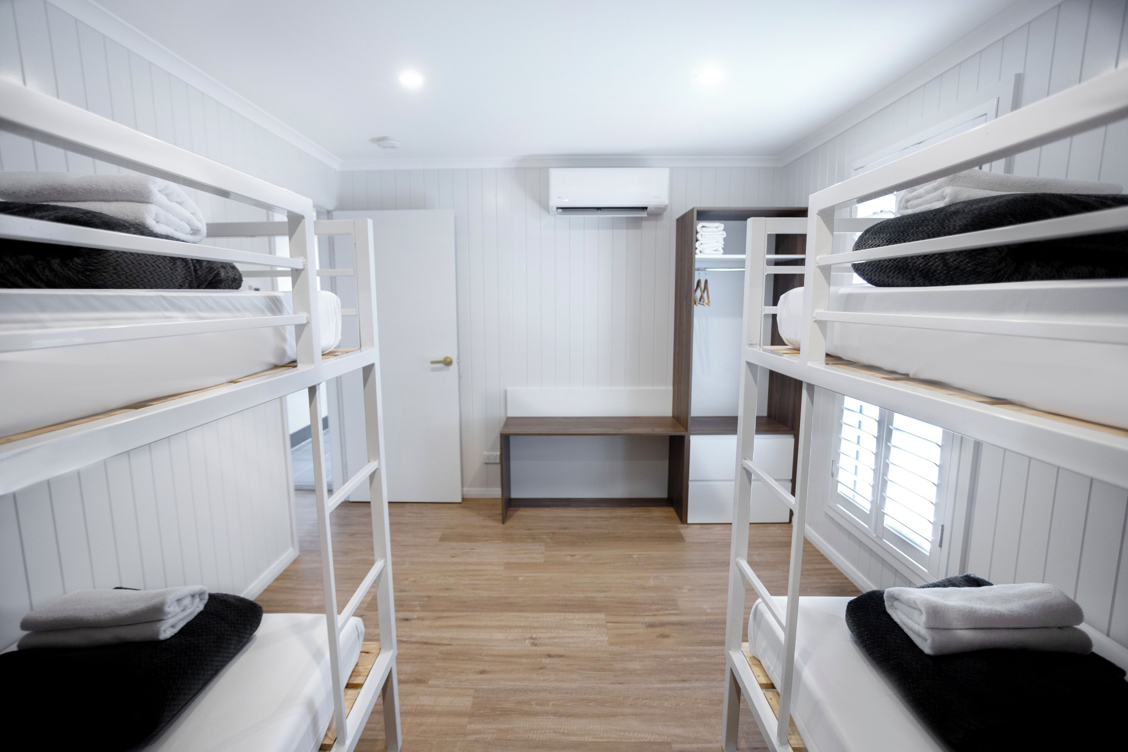 A bunk bed room with white walls, a wooden floor, and a central bench.