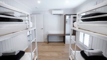 A bunk bed room with white walls, a wooden floor, and a central bench.