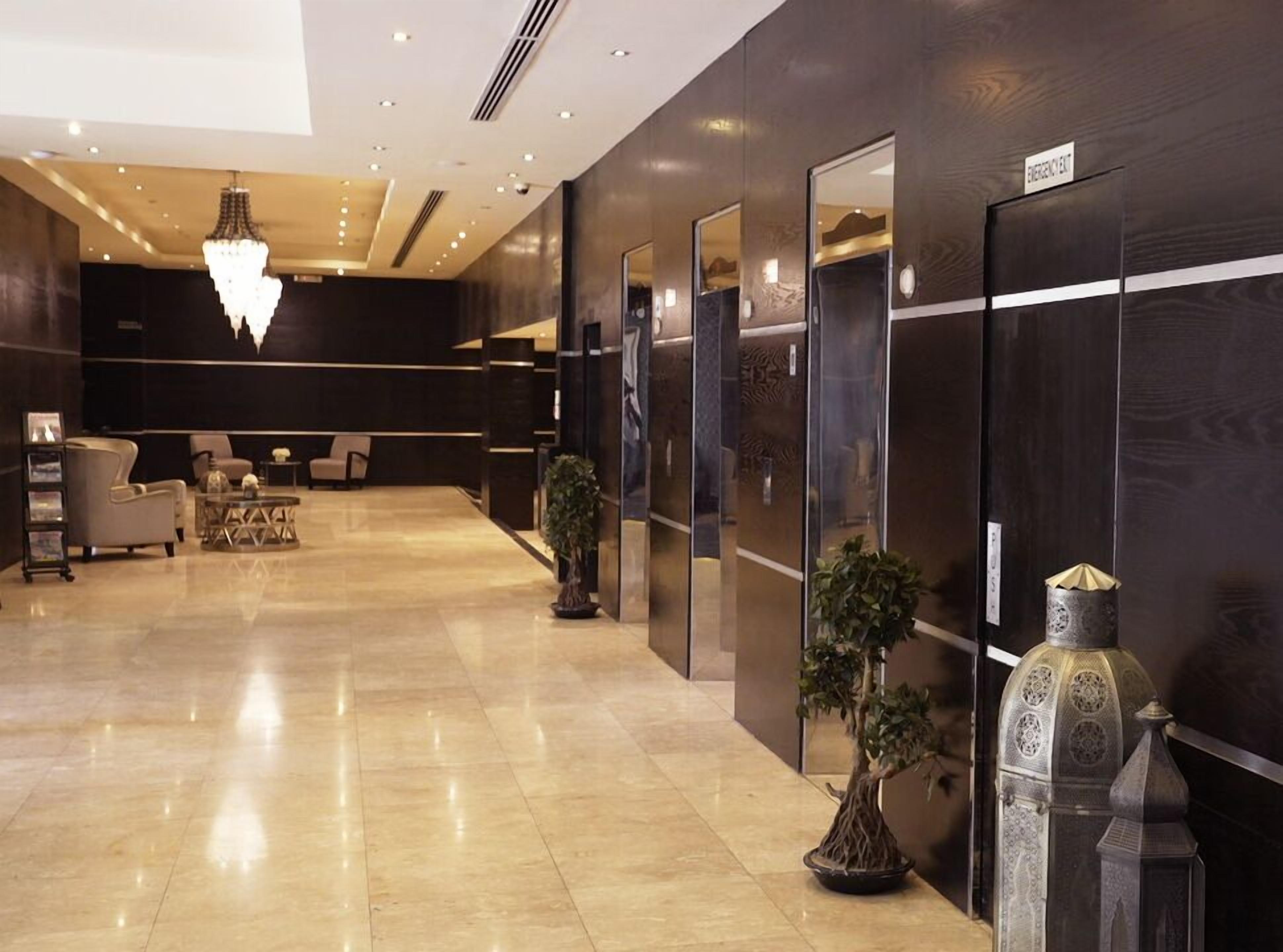 A lobby with a chandelier, seating area, potted plants, and a reception desk.